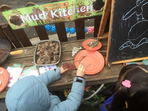 Two pupils from Nursery are pictured wearing their winter coats outdoors, as they play with some pine cones they have collected from the academy grounds.