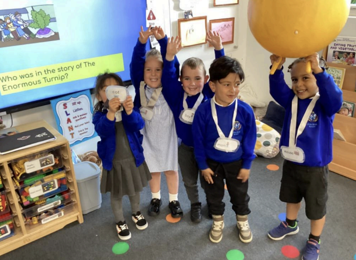 A group of five Nursery pupils are pictured smiling for the camera, as they learn about the story of 'The Enormous Turnip' in class.