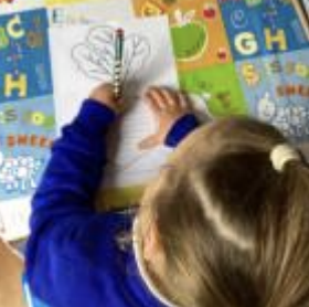 A young girl from Nursery is pictured drawing a picture of a Turnip, whilst sat at her desk.