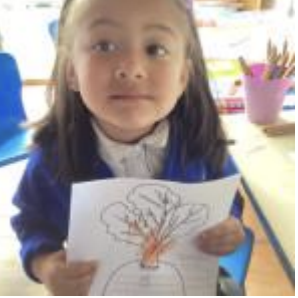 A female Nursery pupil is pictured smiling for the camera, whilst holding up a drawing of a Turnip she has drawn.