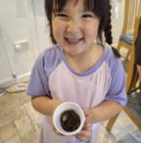 A young girl from Nursery is pictured smiling brightly for the camera, whilst holding a plant pot in her hands.