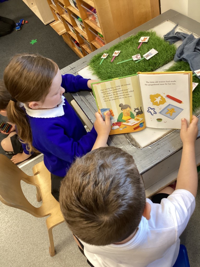 two children, one in a blue checkered dress, reading the "The Gingerbread Man" book together, with illustrations of the story visible on the pages.