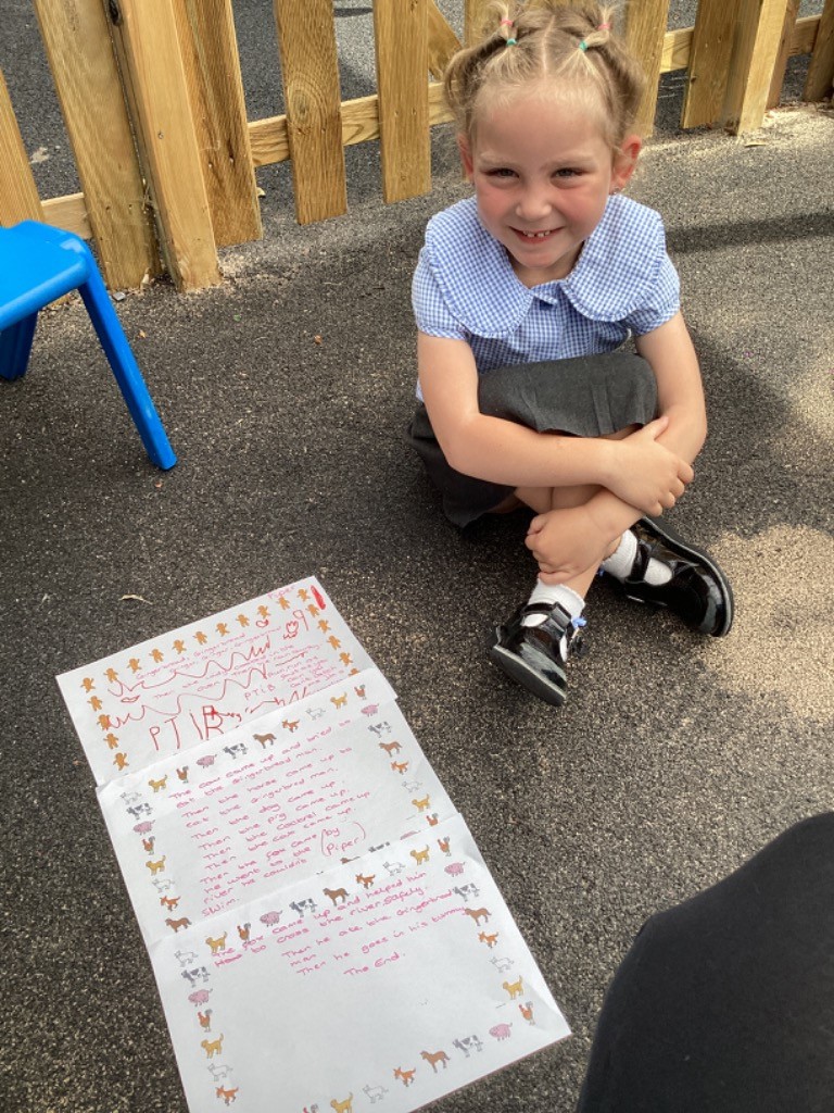 Image features a young girl, possibly a student, sitting on the ground next to a large piece of paper that appears to be a handwritten story or retelling of "The Gingerbread Man." The text is surrounded by small drawings of farm animals, which are characters in the story. This suggests a creative writing or story retelling activity done by the children.