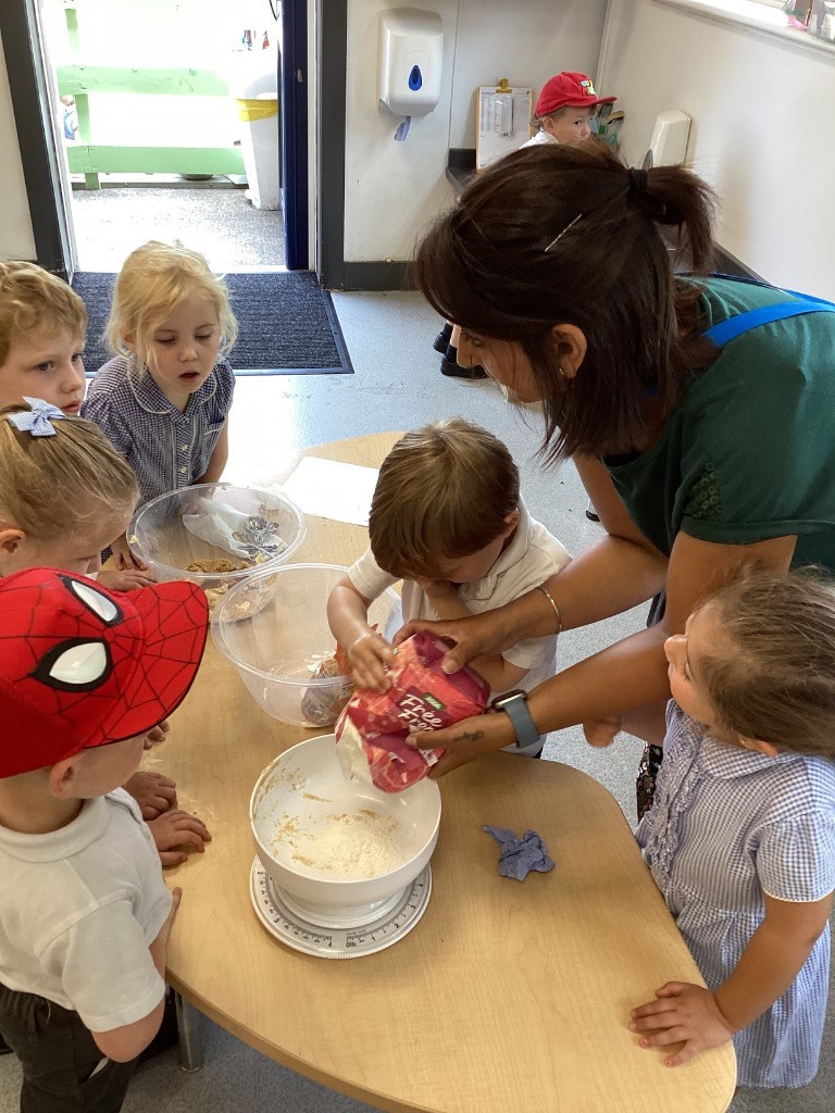 This picture captures children engaged in cooking. In Gingerbread2.jpg, a group of children, including one in a Spider-Man hat, are gathered around a table with an adult. They appear to be mixing ingredients, with one child pouring flour into a bowl on a scale. Gingerbread3.jpg shows a closer view of the same activity, with an adult helping a child pour from a bag into a bowl.