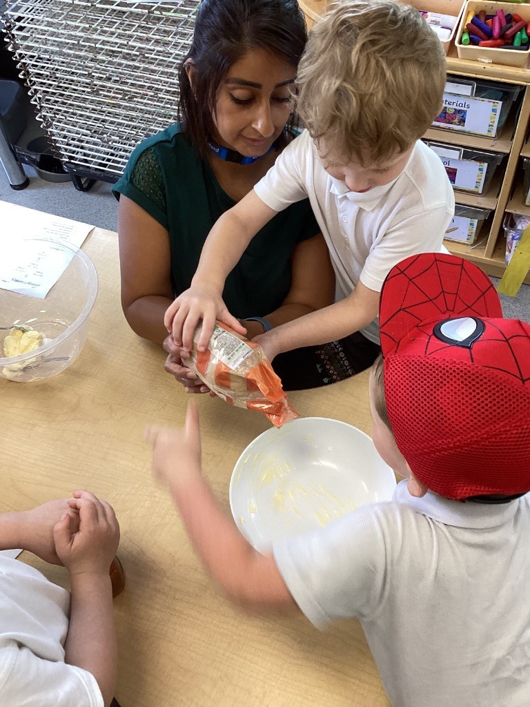 This picture captures children engaged in cooking. In Gingerbread2.jpg, a group of children, including one in a Spider-Man hat, are gathered around a table with an adult. They appear to be mixing ingredients, with one child pouring flour into a bowl on a scale. Gingerbread3.jpg shows a closer view of the same activity, with an adult helping a child pour from a bag into a bowl.