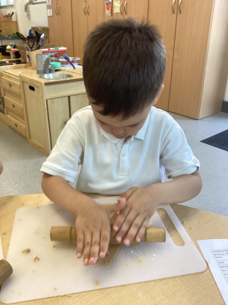 A child, in a school setting, using a rolling pin on dough.