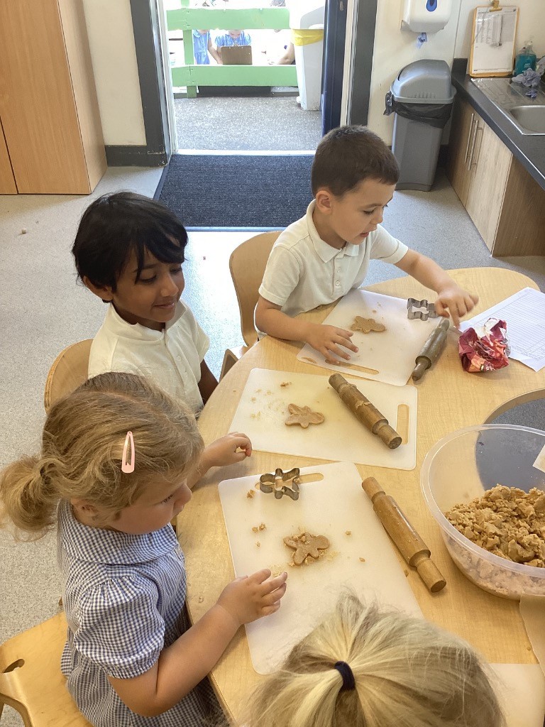 multiple children at a table with rolling pins and cookie cutters, with various shapes already cut out.
