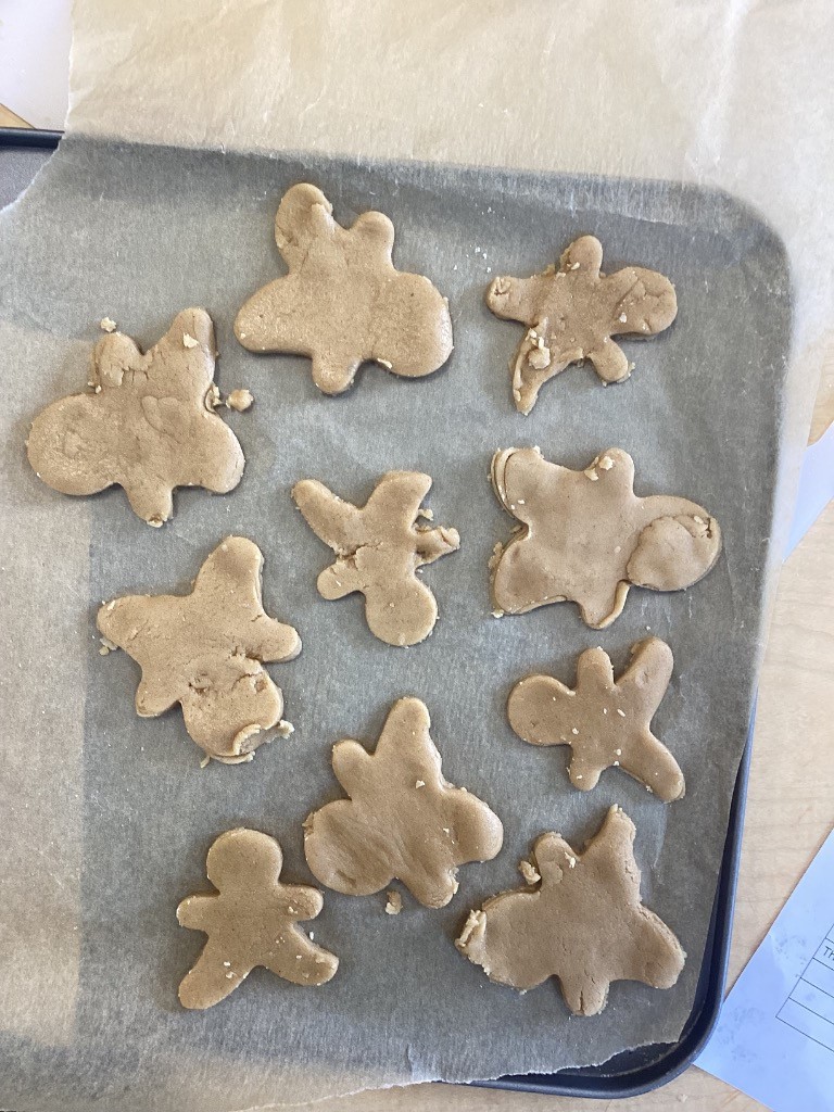 a baking tray with several cut-out gingerbread shapes, ready for baking. Some are clearly gingerbread men, while others are different shapes like butterflies.