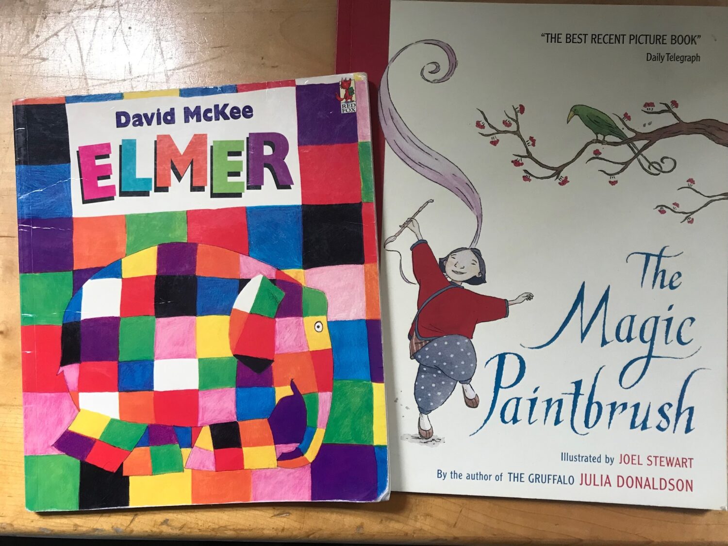 Two children's books are displayed. The book on the left is "Elmer" by David McKee, showing a patchwork elephant. The book on the right is "The Magic Paintbrush" by Julia Donaldson, illustrated by Joel Stewart, depicting a person holding a paintbrush with a long, flowing stroke.