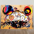 This image shows a large, colorful artwork resembling a stylized, abstract face or character with a wide, smiling mouth. It has large, round shapes at the top that look like ears, and the artwork features many swirling, eye-like elements and bright colors on a beige background.