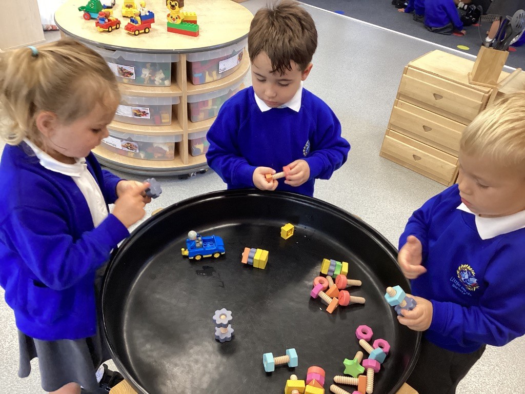 three children are playing together at a black sensory table with various colorful blocks and toys.