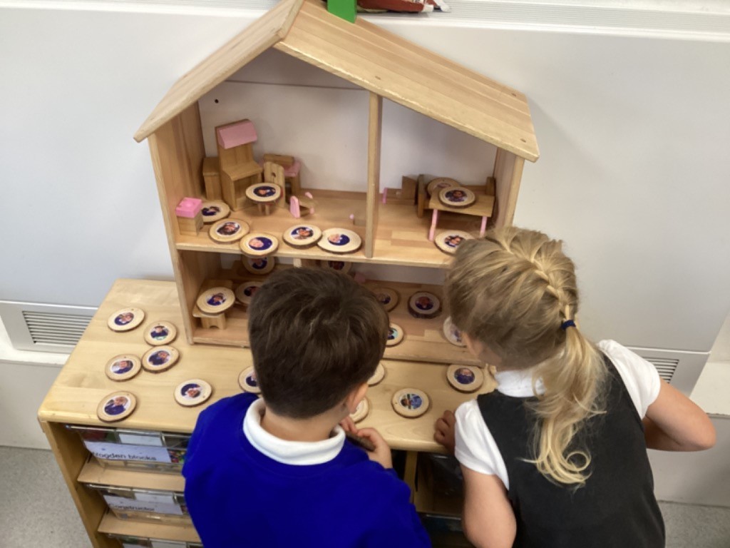 children are using a wooden dollhouse with round wooden tokens that have pictures of people on them, likely to represent different family members or characters.