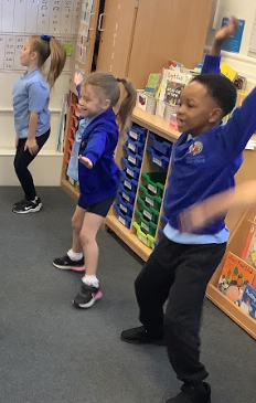 children are participating in a group exercise or dance activity, raising their hands and moving their bodies. This looks like a physical education or warm-up activity.