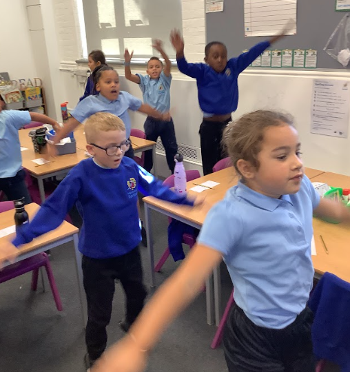 children are participating in a group exercise or dance activity, raising their hands and moving their bodies. This looks like a physical education or warm-up activity.