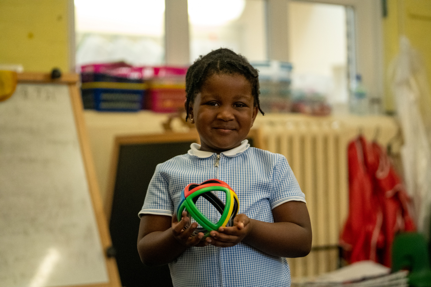 A young black girl holding a rainbow ball wearing a blue summer dress.