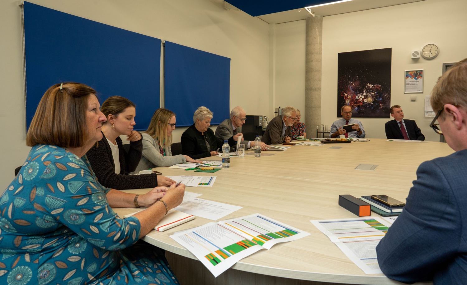 Governors seen meeting with several people sat round a large table in a boardroom.