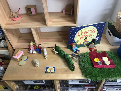 A copy of the children's storybook 'Chapatti Moon' is seen standing on a wooden cabinet, along with some figures of people and farm animals from the story.