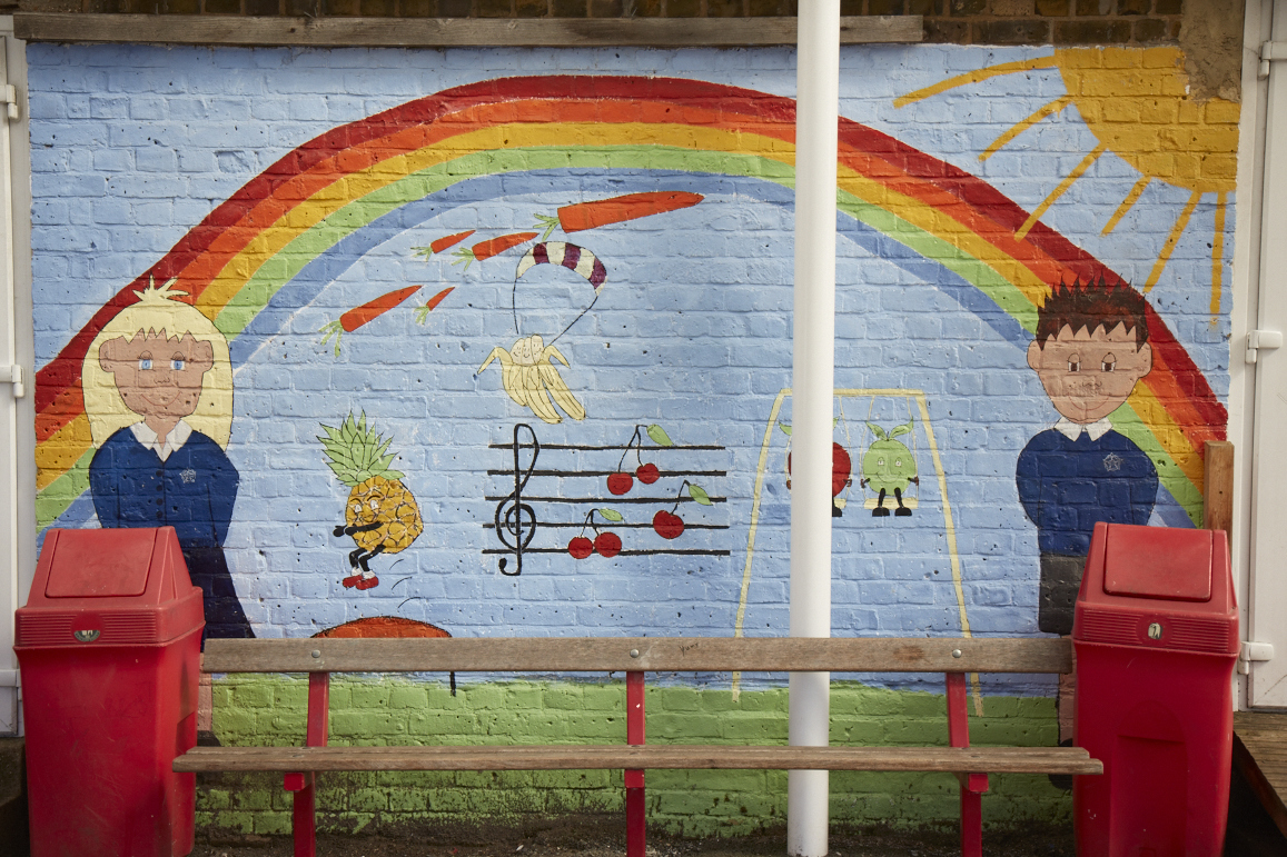 An external brick wall is pictured featuring a painted mural of two DPA pupils stood at either end of a large field, with a rainbow and various other images visible behind them.