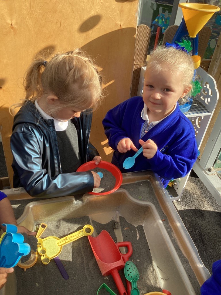 two children are playing together in a sand or sensory tray with shovels and other tools.