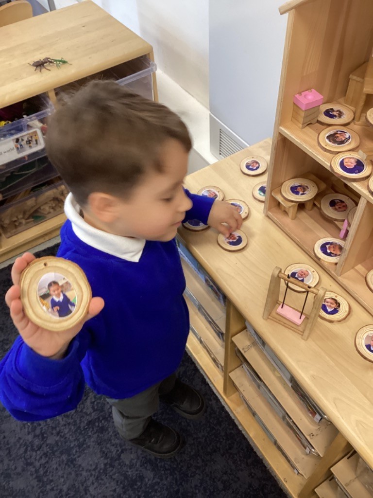 children are using a wooden dollhouse with round wooden tokens that have pictures of people on them, likely to represent different family members or characters.