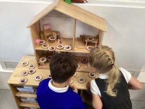 children are using a wooden dollhouse with round wooden tokens that have pictures of people on them, likely to represent different family members or characters.