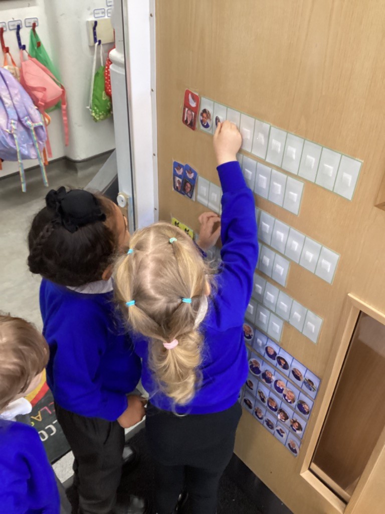 two children are working together, placing small cards on a vertical chart or board.