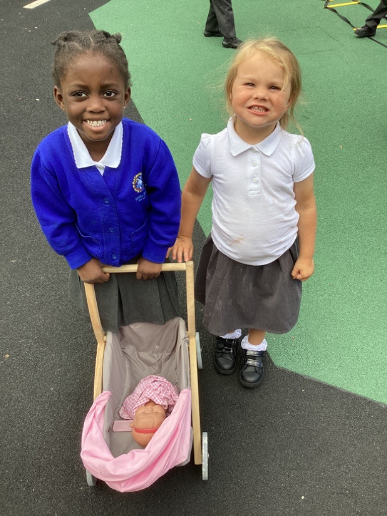 two children are standing together, one is pushing a toy stroller with a doll inside
