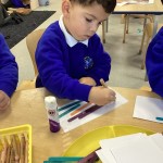 A child is focused on pressing down a set of colorful craft sticks onto a piece of paper, securing them with glue.
