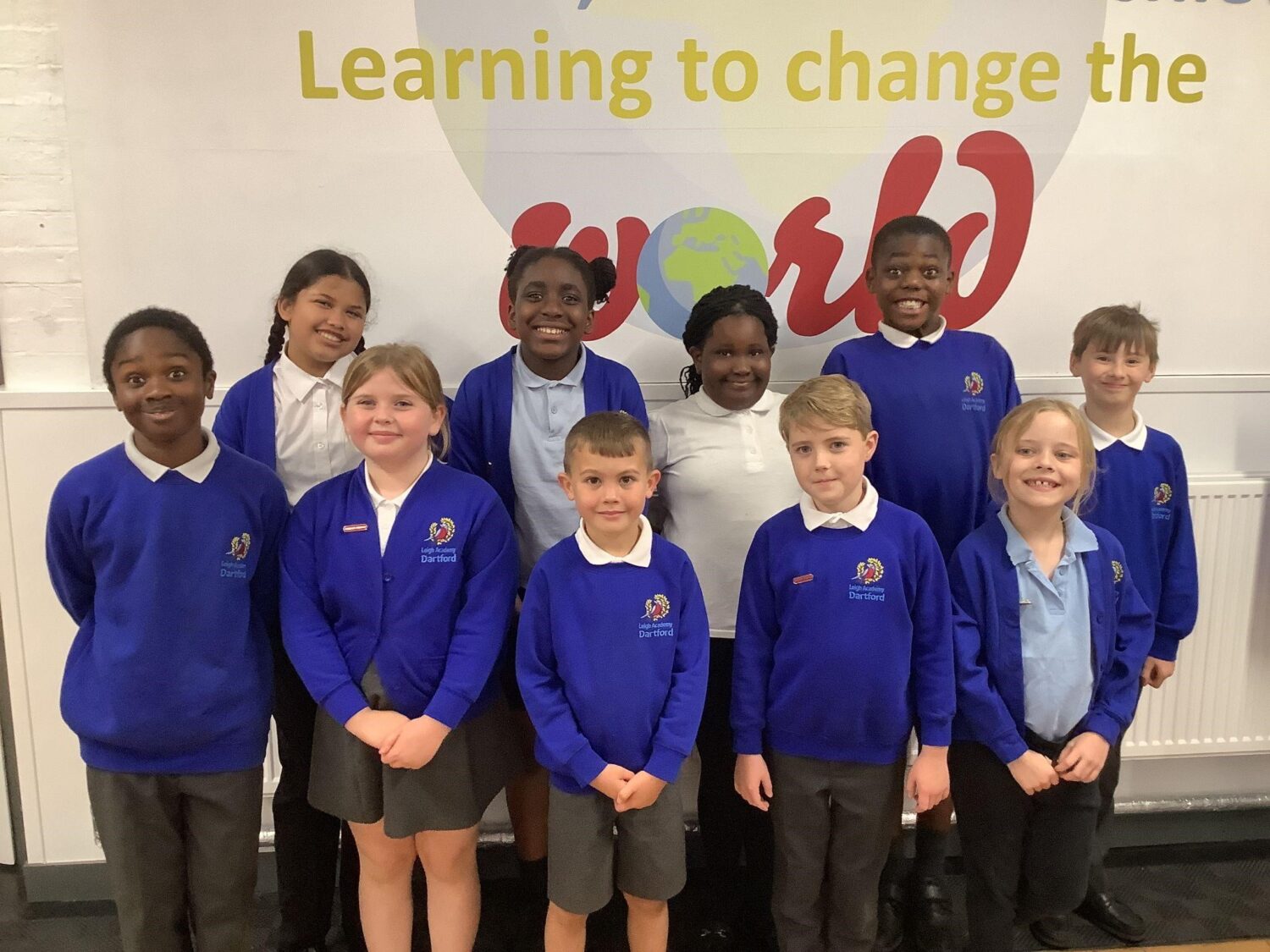 A group of 10 school children standing in front of wall art displaying the wording Learning to change the world.
