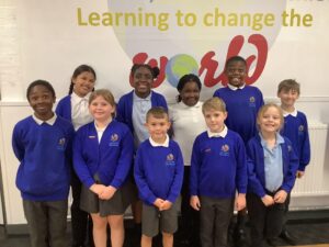 A group of 10 school children standing in front of wall art displaying the wording Learning to change the world.