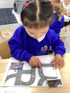 A young child in a blue uniform concentrating on drawing or playing on a paper with a road map design.