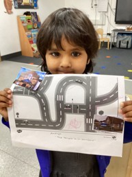 A young child holding up a printed sheet showing a road map diagram with small photos attached.