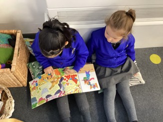 Two girl in blue and grey school uniform sitting on the floor reading a book