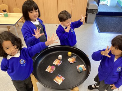 4 young kids in blue and grey uniform stand around a round table holding their hand up showing 5 fingers