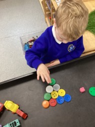 A child in a school uniform arranges colorful plastic counters into a pyramid shape on a black activity tray.