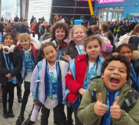 A group of smiling children posing closely together for a photo; one boy in the foreground is cheering with both thumbs up.