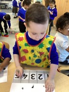 A child wearing a colorful shape-patterned apron works on a counting activity involving numbers 1 through 5.