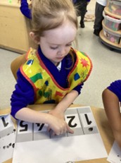 A child wearing a colorful shape-patterned apron works on a counting activity involving numbers 1 through 5.