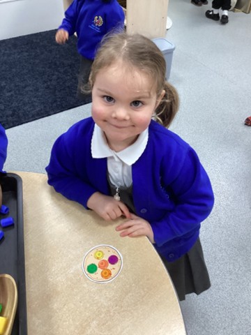 A smiling student stands at a table next to a small circular paper cutout.