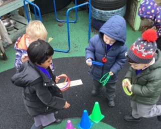 Children in winter coats play a ring toss game outdoors using colorful hoops and cones.