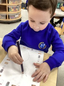 A child sits at a table using a purple pencil to draw on a recycling-themed worksheet.