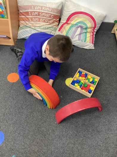 A student sitting on the floor playing with curved wooden rainbow blocks and a sorting box full of colorful counting bears.