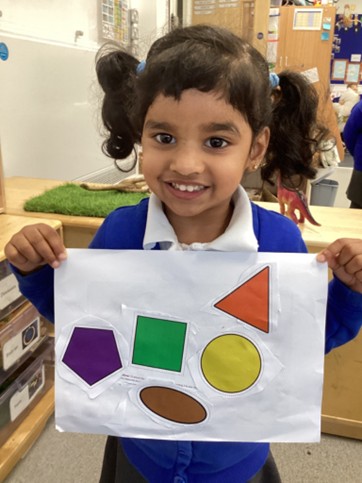A smiling student holding up a piece of paper with large, colorful shapes glued to it.