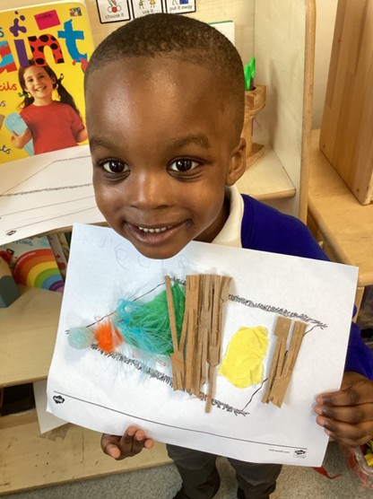 A smiling student holding up a finished craft project made with strips of cardboard, colored tissue paper, and feathers.