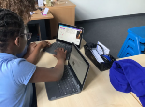 Two children sitting a desk trying on laptops
