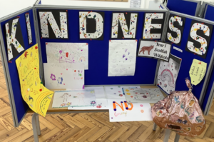 Large letters spelling part of the word “kindness” above a display of pupils’ drawings and posters on blue boards.