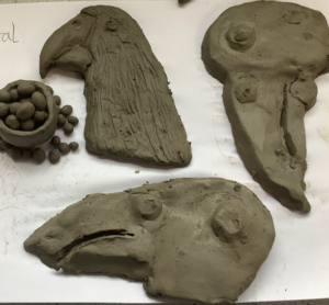 Grey clay sculptures made by pupils, including a bird’s head with a curved beak and a flat textured piece, laid out on a white surface.